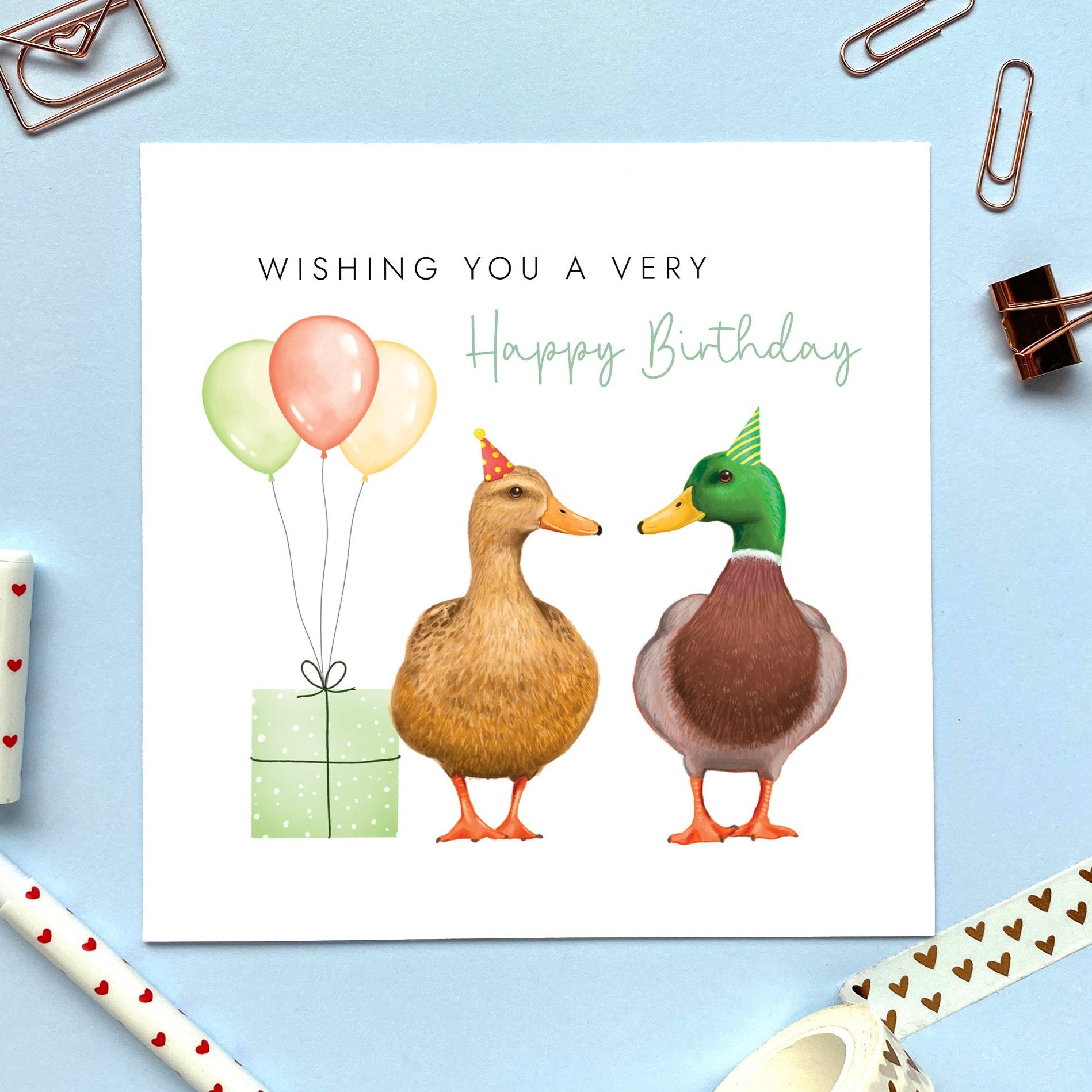 A birthday card featuring two mallard ducks with a green present and balloons. The text says 'Wishing you a very Happy Birthday'.