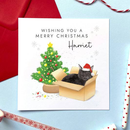 A personalised Christmas card featuring a black cat in a box wearing a santa hat next to a christmas tree. It can be personalised with a name, and is suitable for a range of relations such as Wife, Girlfriend, Daughter, Granddaughter, Niece and Mum.