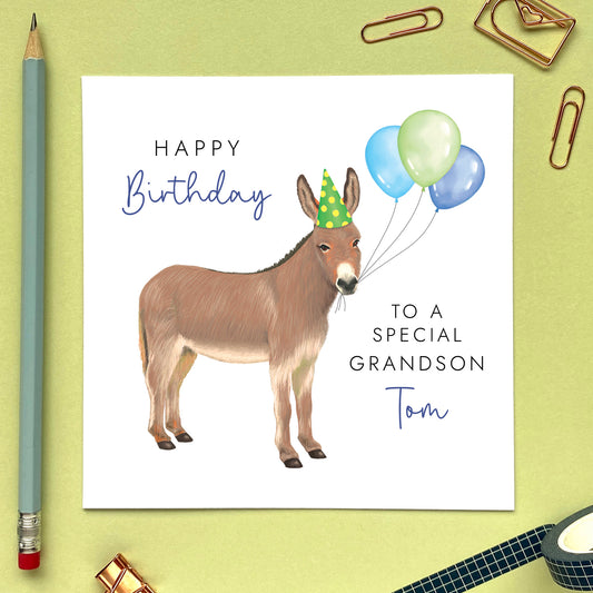 A personalised birthday card for him featuring a donkey with birthday balloons. It can be personalised with a name, relation and any age. The card in the photo is a birthday card for Grandson.