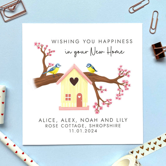 A personalised New Home card featuring two blue tits sitting on a blossom tree branch and a cream birdhouse. It says 'wishing you happiness in your new home'. It can be customised with names, address and moving date.