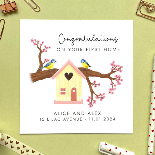 A personalised congratulations on your first home card. The design features two blue tits sitting on a blossom tree branch with a cream birdhouse. It can be customised with names, address and moving date.