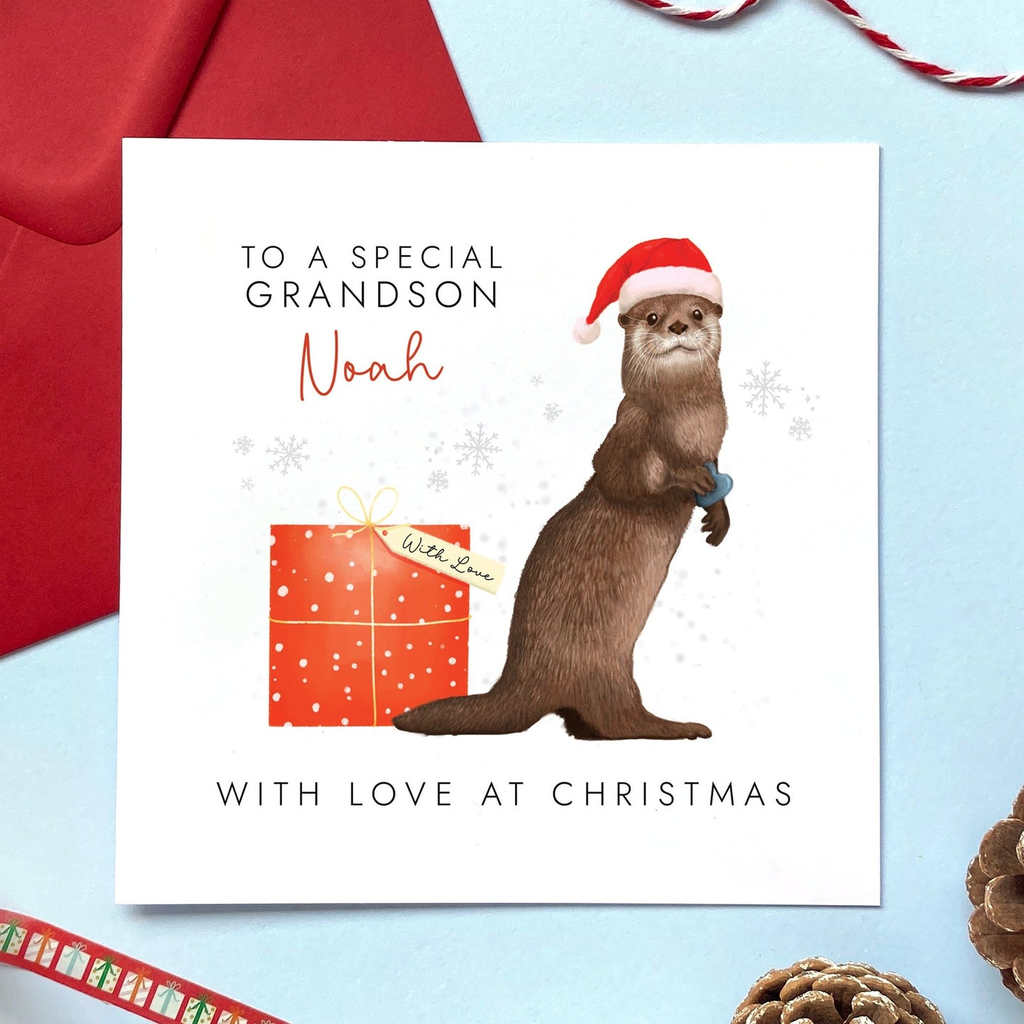 A personalised Christmas Card for Boy featuring a brown otter in a Santa hat. The card in the photo is a Christmas Card for Grandson.