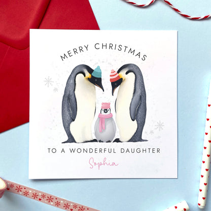 A personalised Christmas Card for Girl featuring two adult penguins and a baby penguin wearing a pink scarf. It can be personalised with a name. The card in the photo is a Christmas Card for Daughter.