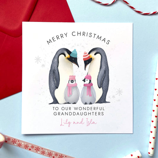 A personalised Christmas Card for Granddaughters. It features two parent parents and two baby penguins to represent two girls, children, babies or twins. It can be personalised with their names.