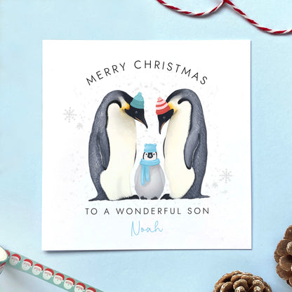 A personalised Christmas Card for Grandson featuring two parent penguins and a baby penguin wearing a blue scarf. It can be customised with a name. The card in the photo is a Christmas Card for Son.