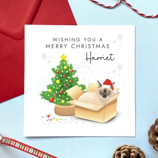 A personalised Christmas card featuring a siamese cat in a box wearing a santa hat next to a christmas tree. It can be personalised with a name, and is suitable for a range of relations such as Wife, Girlfriend, Daughter, Granddaughter, Niece and Mum.